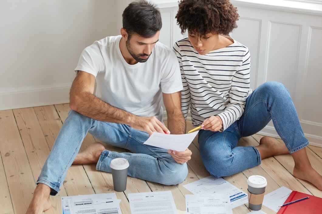 Couple sitting on the floor surrounded by paperwork and coffee, engaged in discussion and planning together
