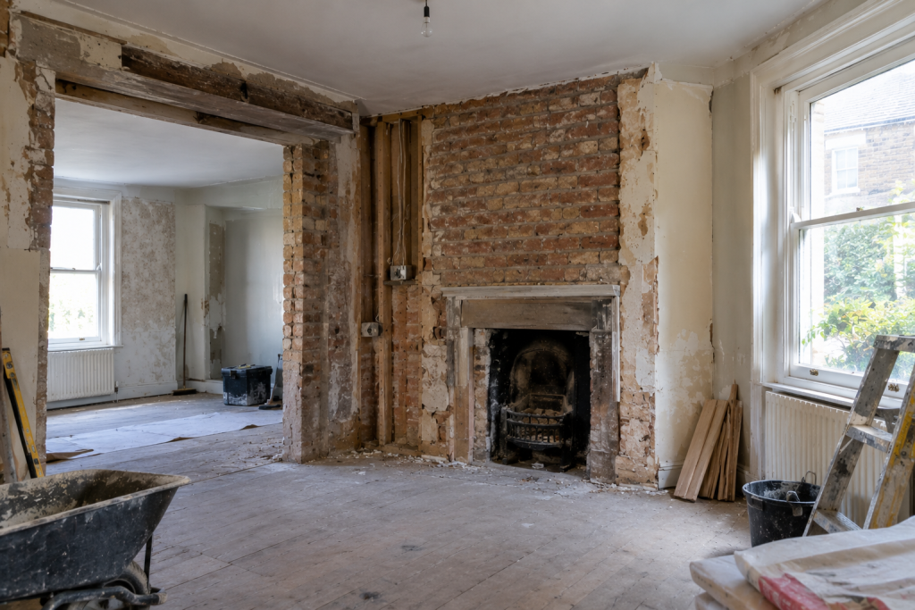 House undergoing renovation with exposed brick fireplace and wooden floors in a sunlit room